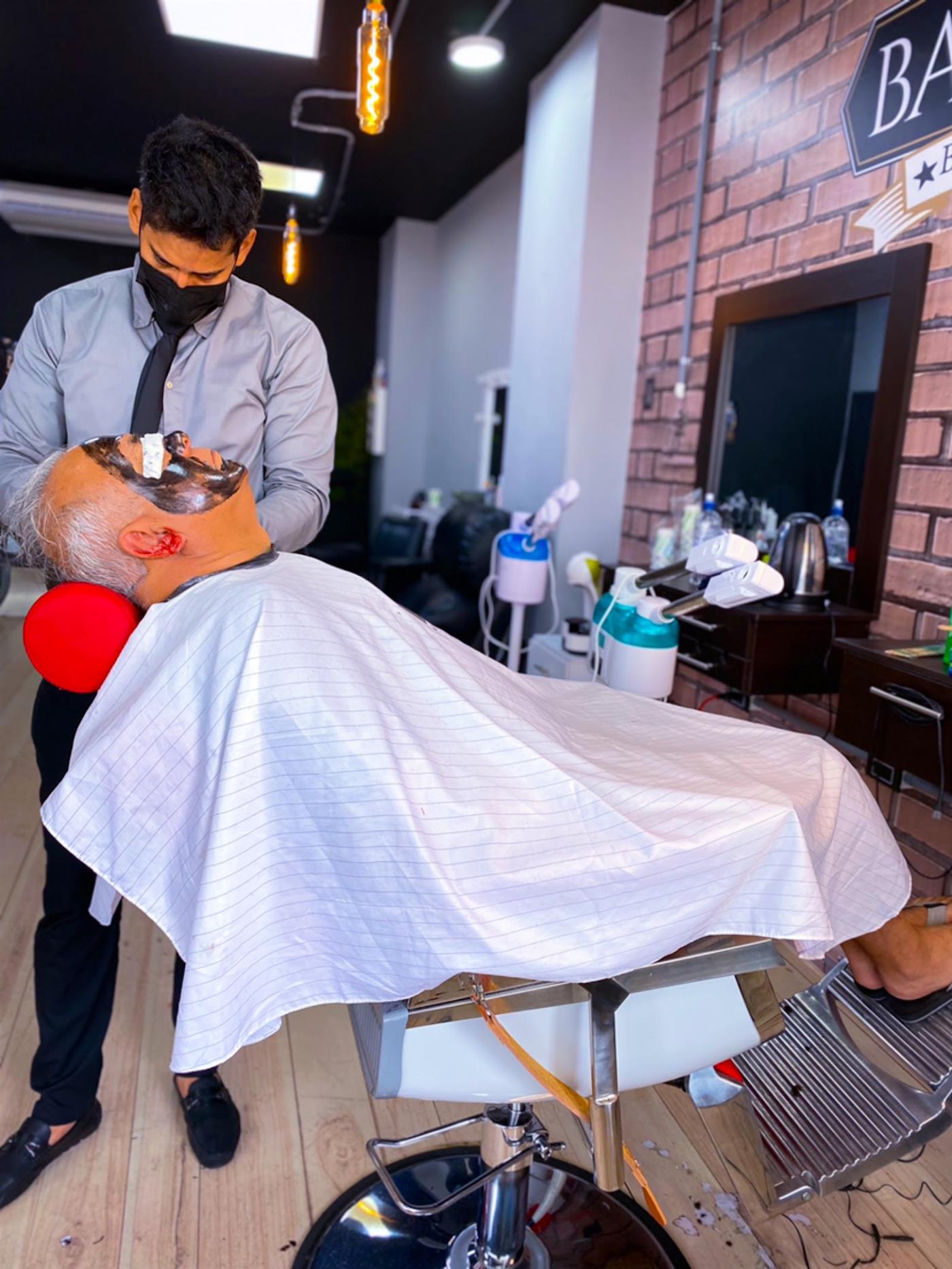 Barbero haciendo un cuidado de rostro a un cliente reclinado