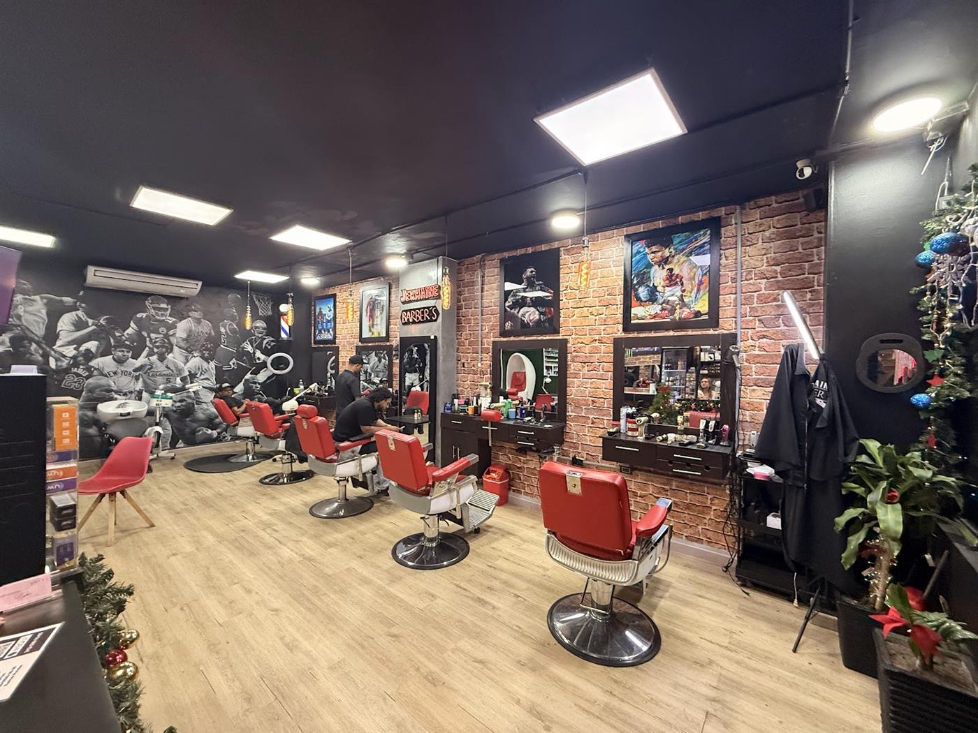 Interior de la barbería con sillones rojos, pared de ladrillo y mural en blanco y negro